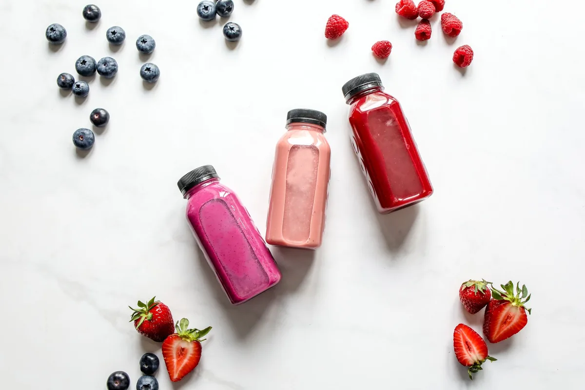 Bananas, strawberries and blueberries laid out on a light wooden board beside a glass of milk