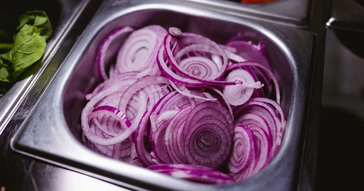 Sliced red onions in a steel prep pan