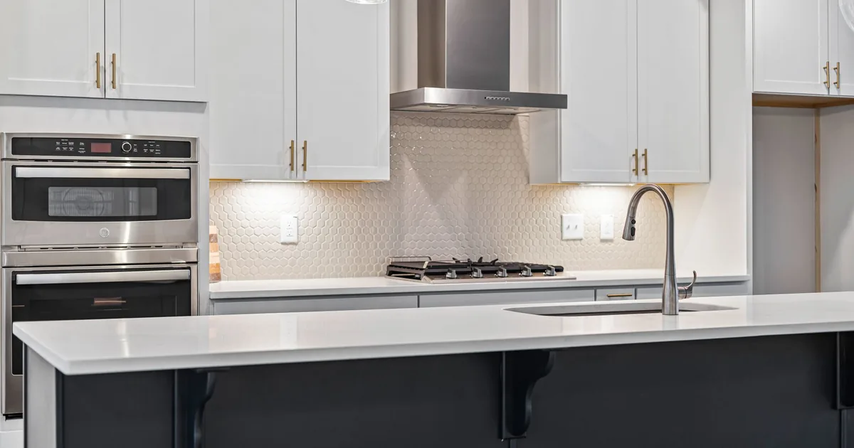 A white kitchen with a chimney hood, wall ovens and an island