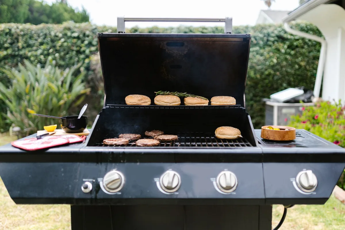 Burger patties cooking on a black gas grill with its lid open in a garden