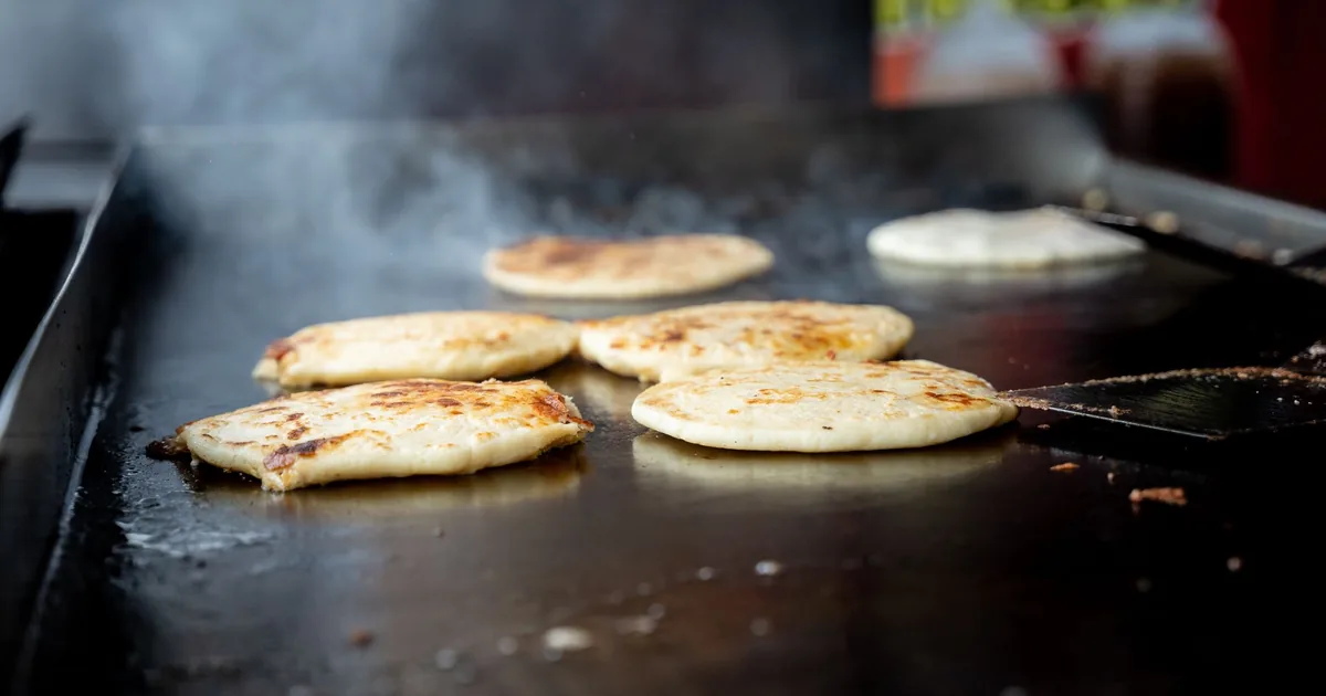 Pancakes cooking on a large outdoor flat-top griddle with light steam rising