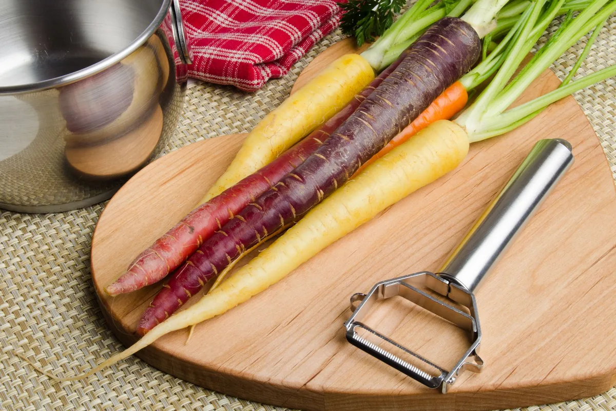 Rainbow carrots and a peeler on a wooden board
