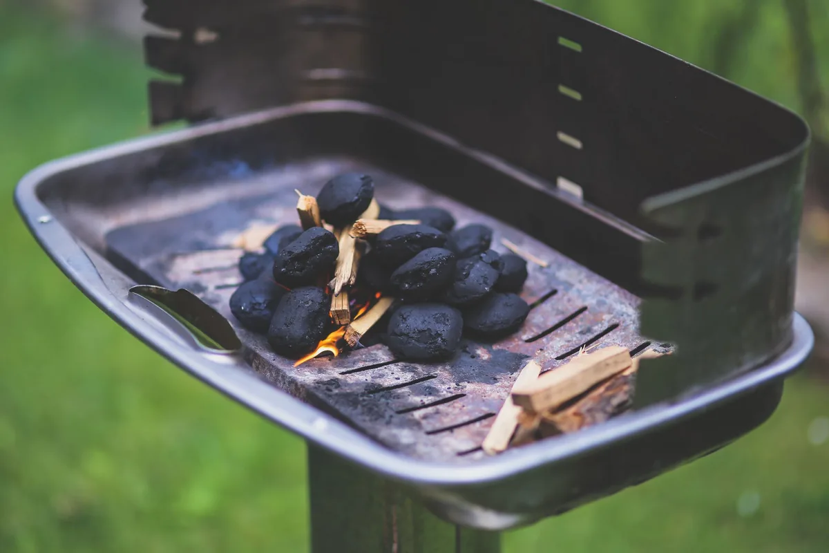 Charcoal briquettes lit in a small portable grill on grass