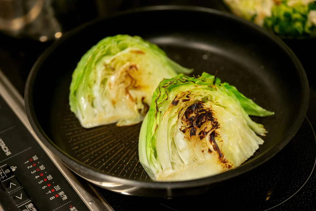 Charred cabbage wedges in a dark pan on an induction hob