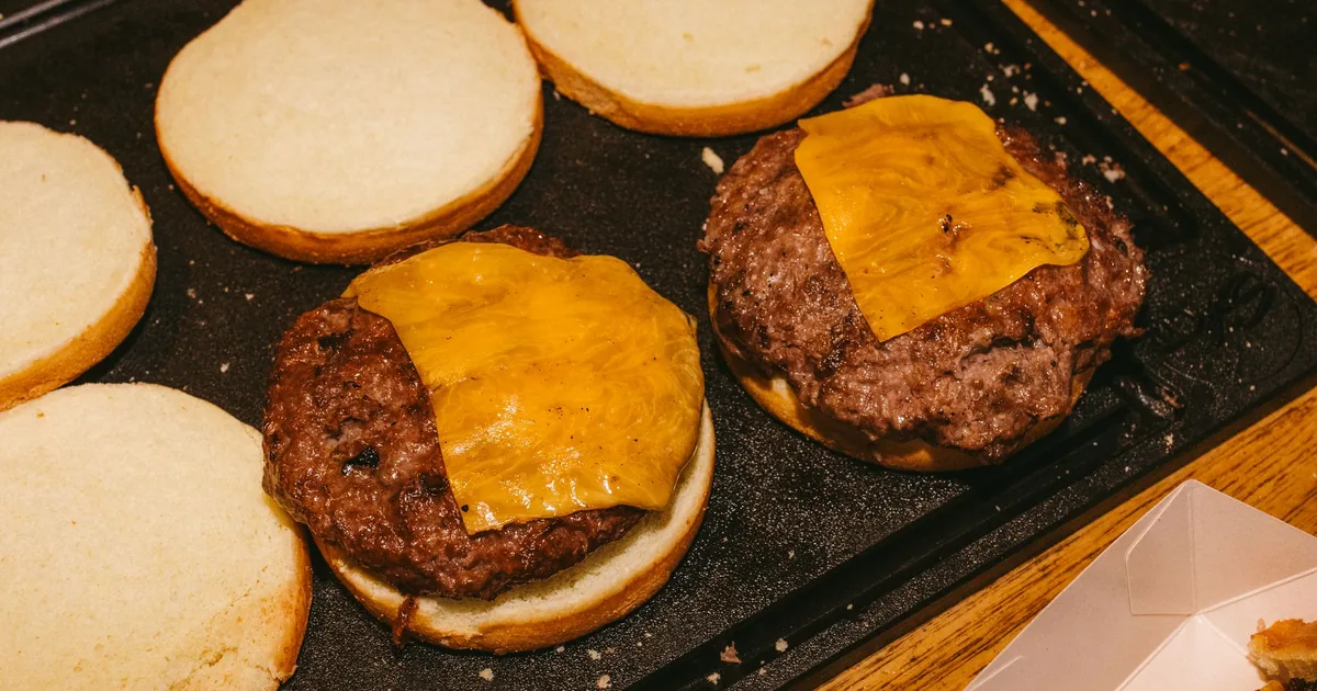 Cheeseburger patties with melted cheese on a griddle beside open buns