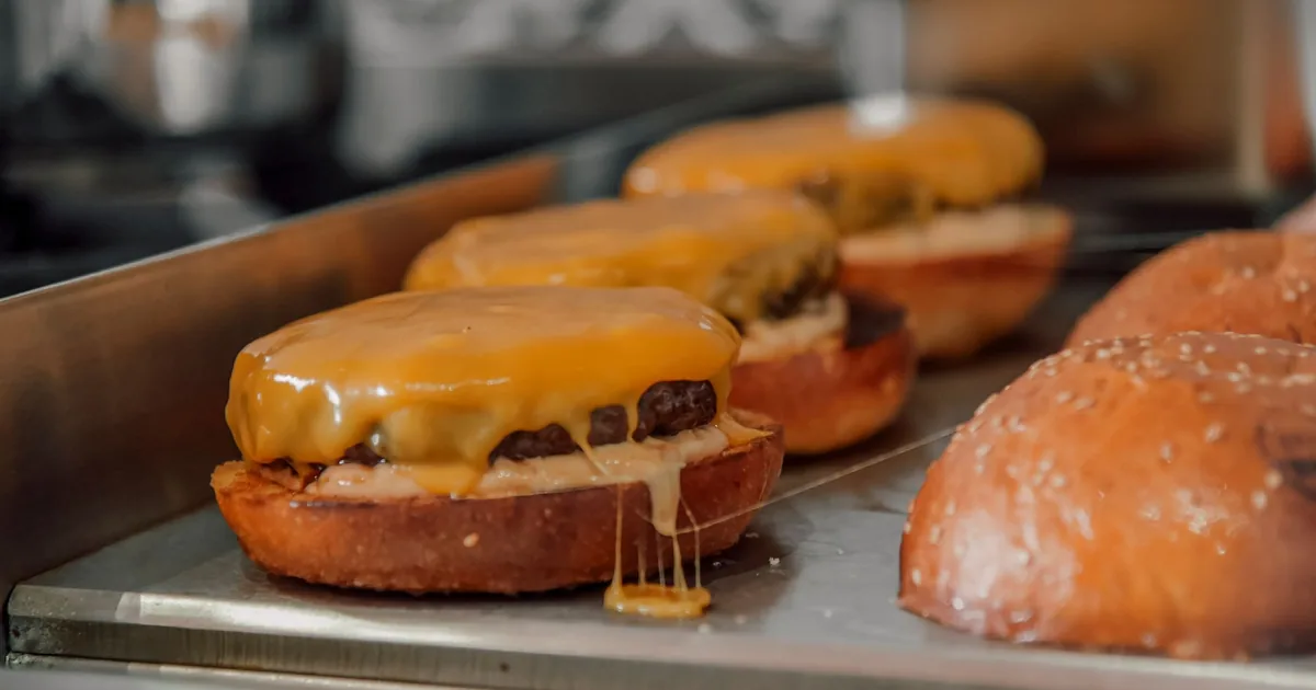 Cheeseburgers with melted cheese cooking on a flat-top griddle beside toasted buns