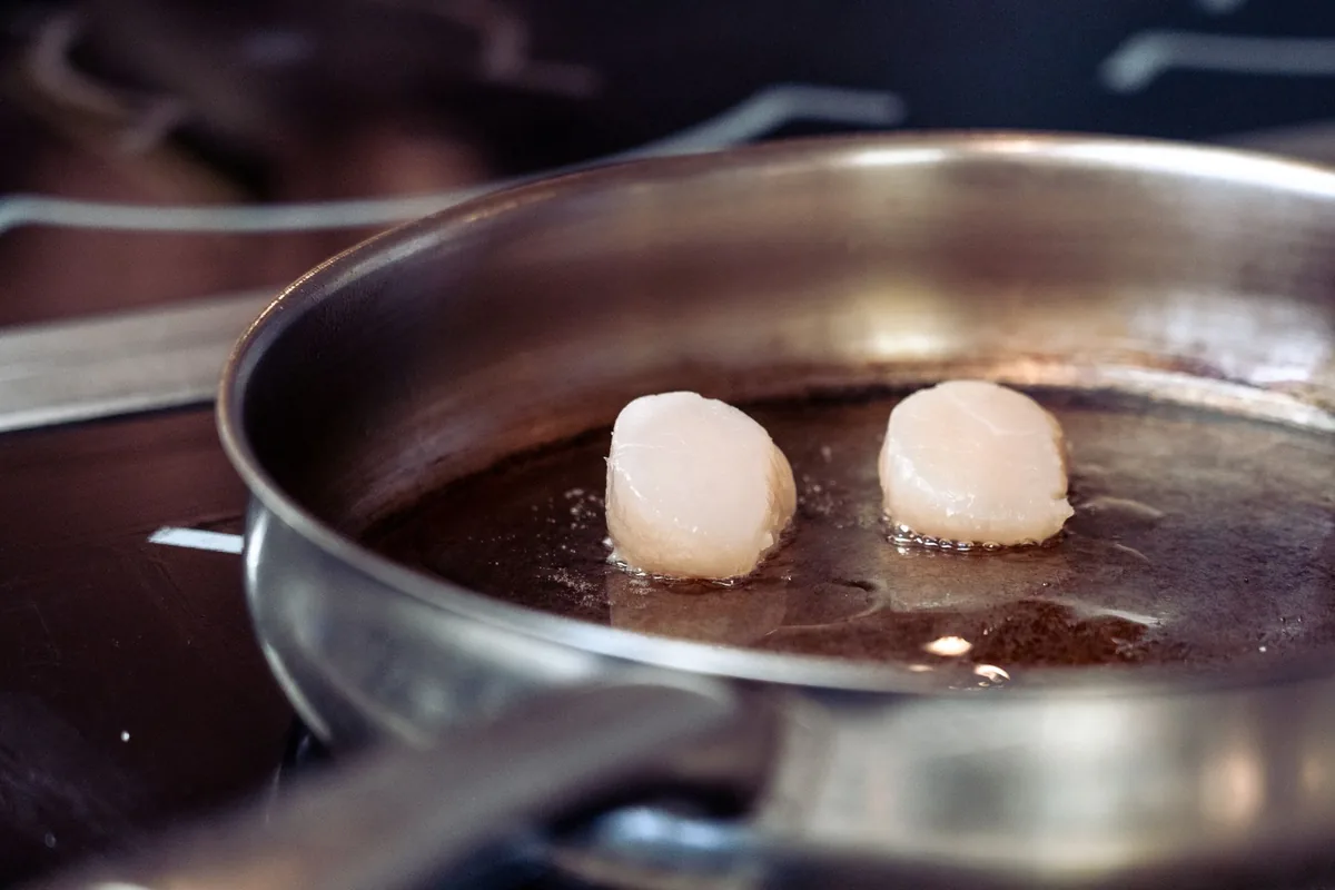 Two scallops searing in a stainless steel pan