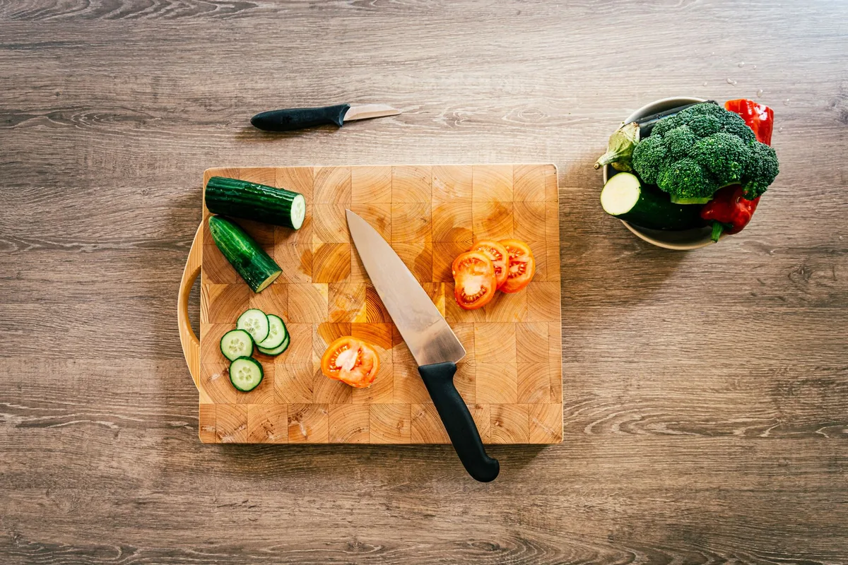 Chopped vegetables and a knife on a wooden board, seen from above