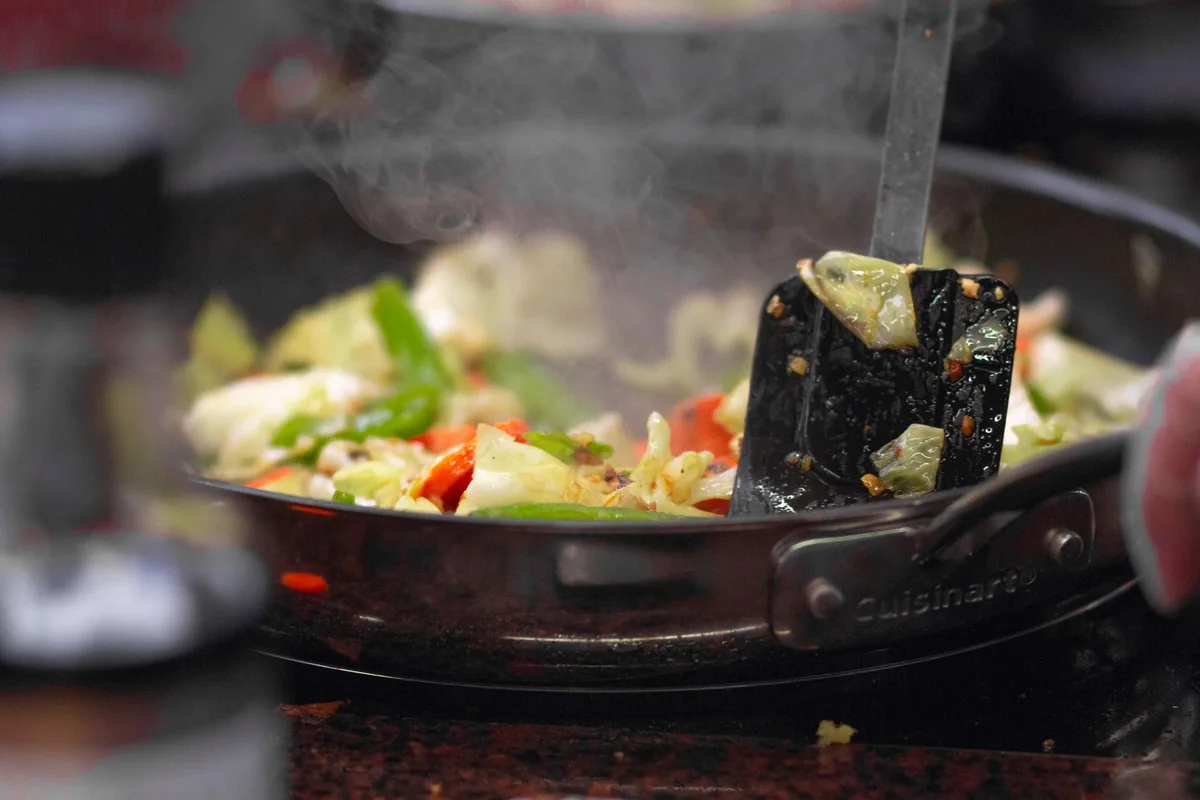 Chopped vegetables cooking in a dark nonstick saute pan on a hob