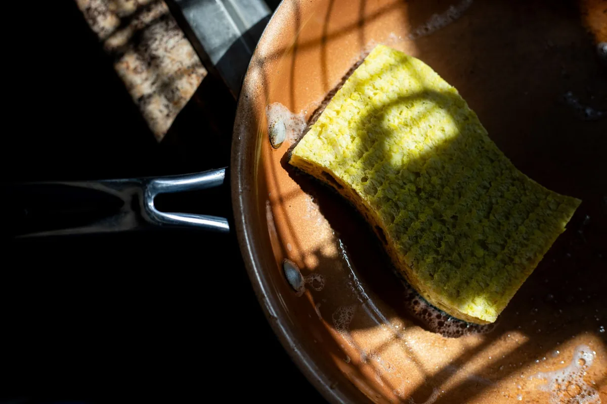 A sponge scrubbing the inside of a copper-coloured pan