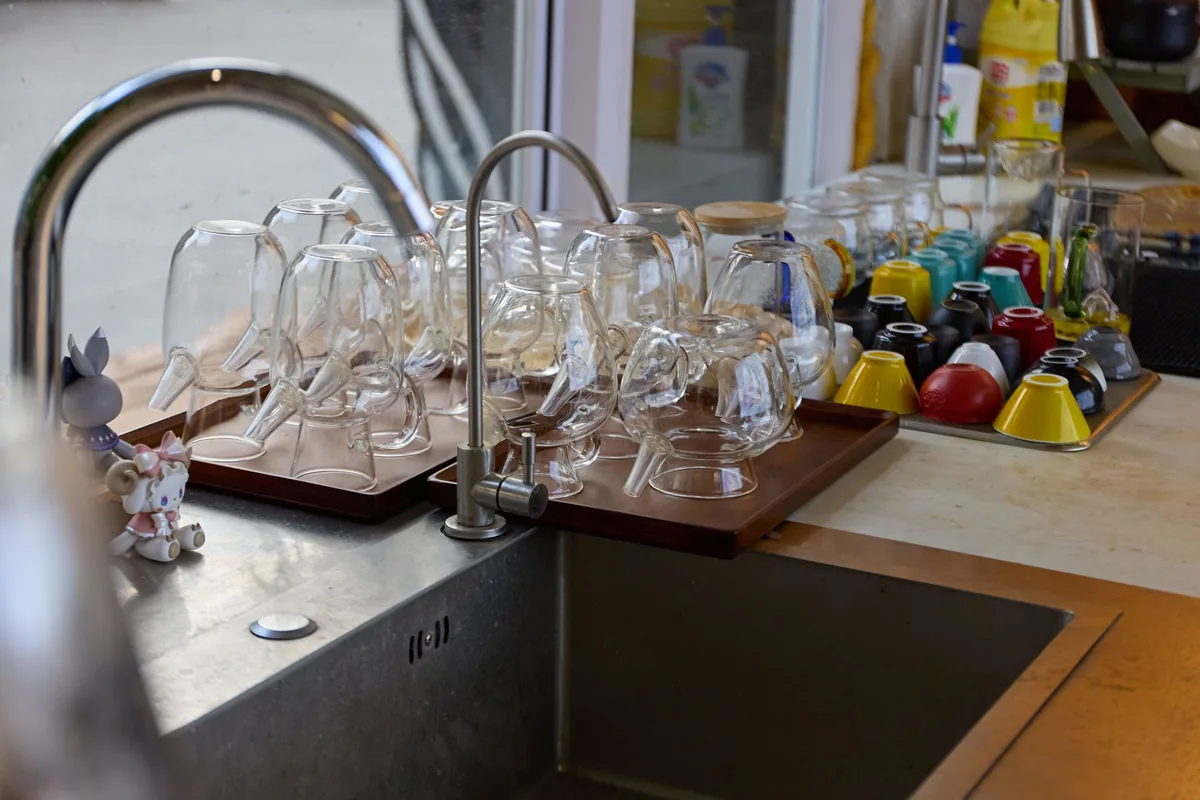 Clean plates and glasses drying in a rack beside a kitchen sink