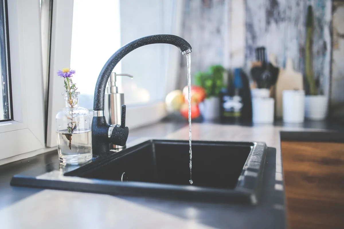 Water running from a black faucet into a dark sink