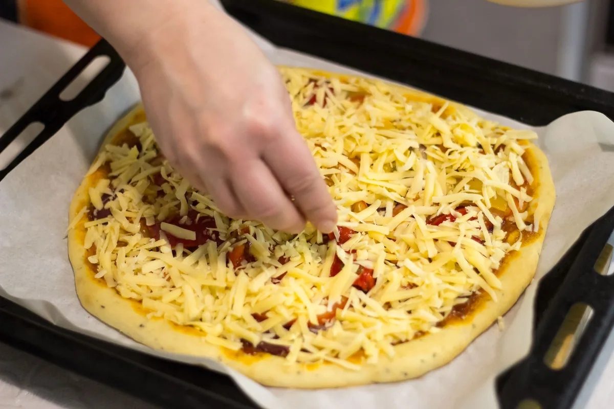 Cheese being scattered over a pizza before baking