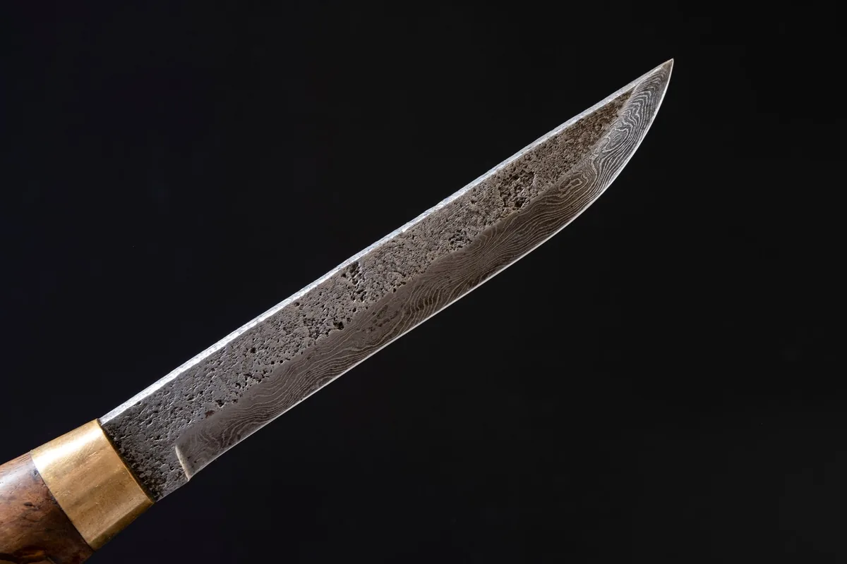 Close view of a knife blade with a rippled layered steel pattern