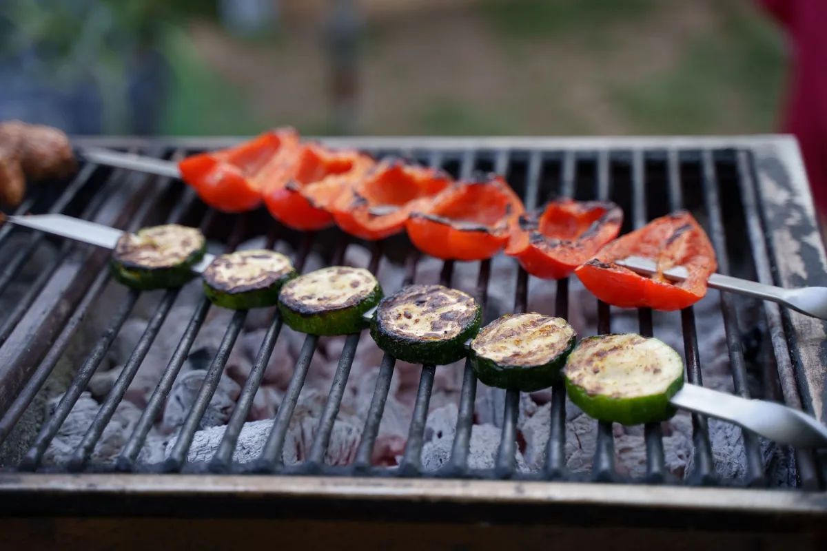 Colourful vegetable skewers browning side by side on a barbecue grate