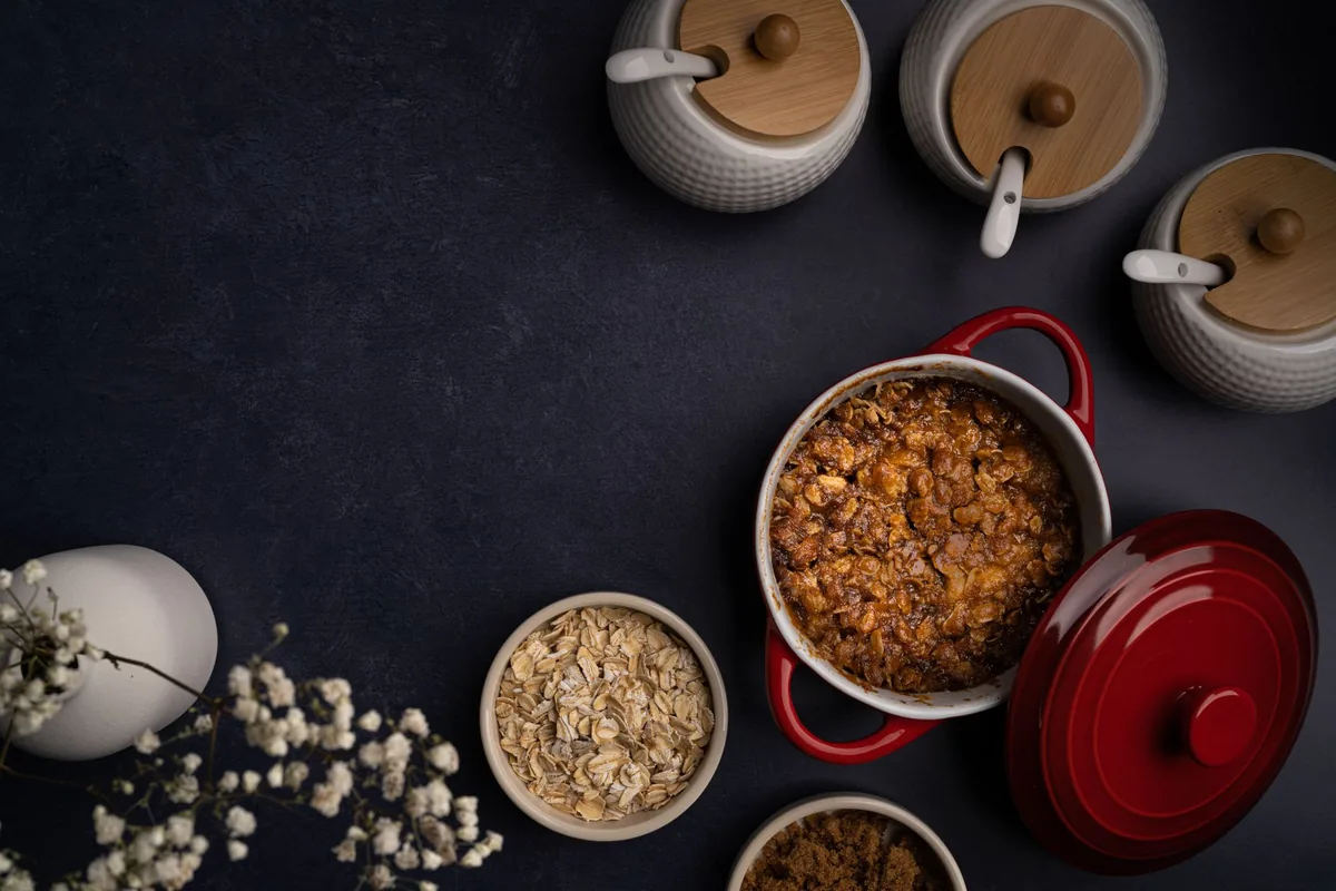 A red casserole of grains among bowls on a dark table