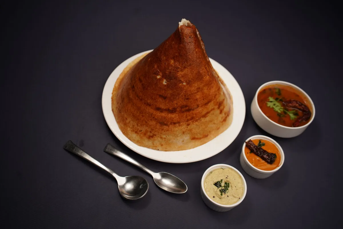 Crisp dosa and soft white idli on a plate with small bowls of chutney and sambar