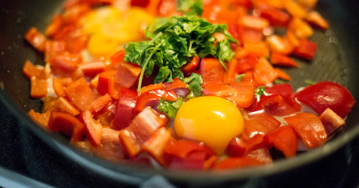 Eggs and peppers cooking in a wide pan