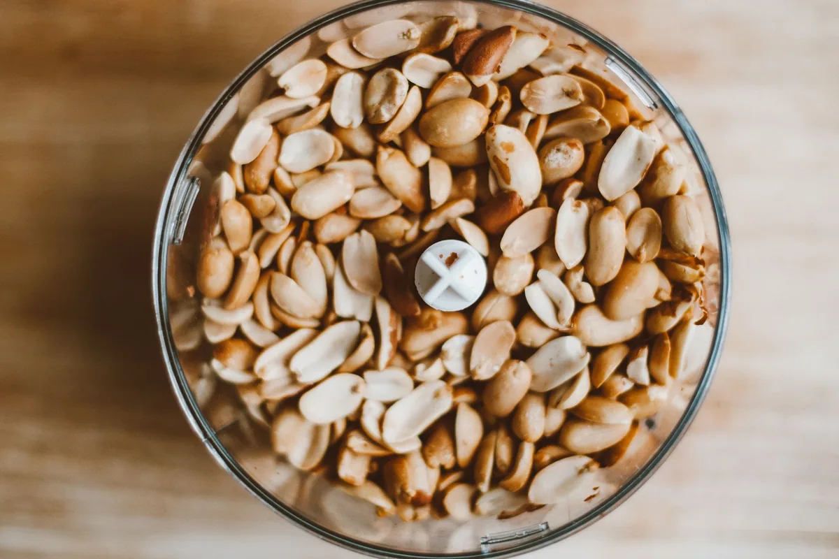 Halved peanuts in a clear food processor bowl, seen from above