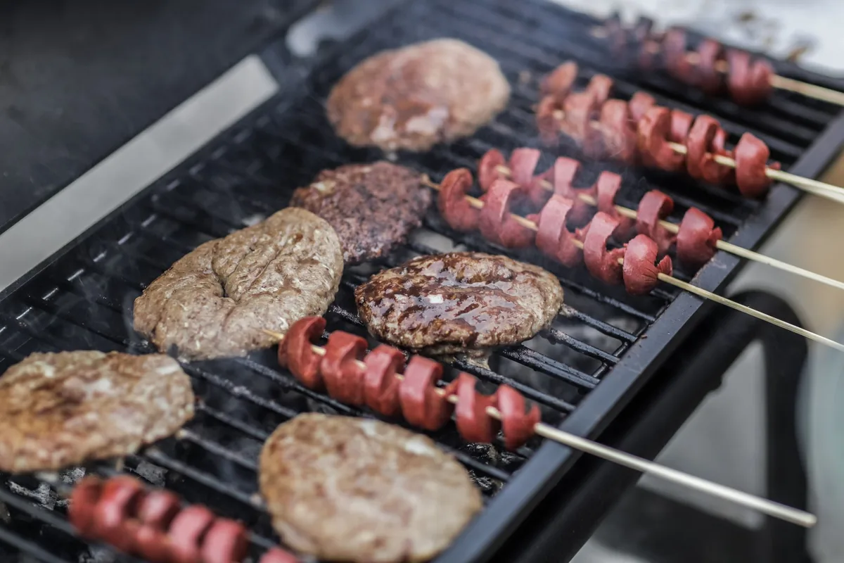 Burger patties and spiral-cut sausages on skewers grilling on a compact grate