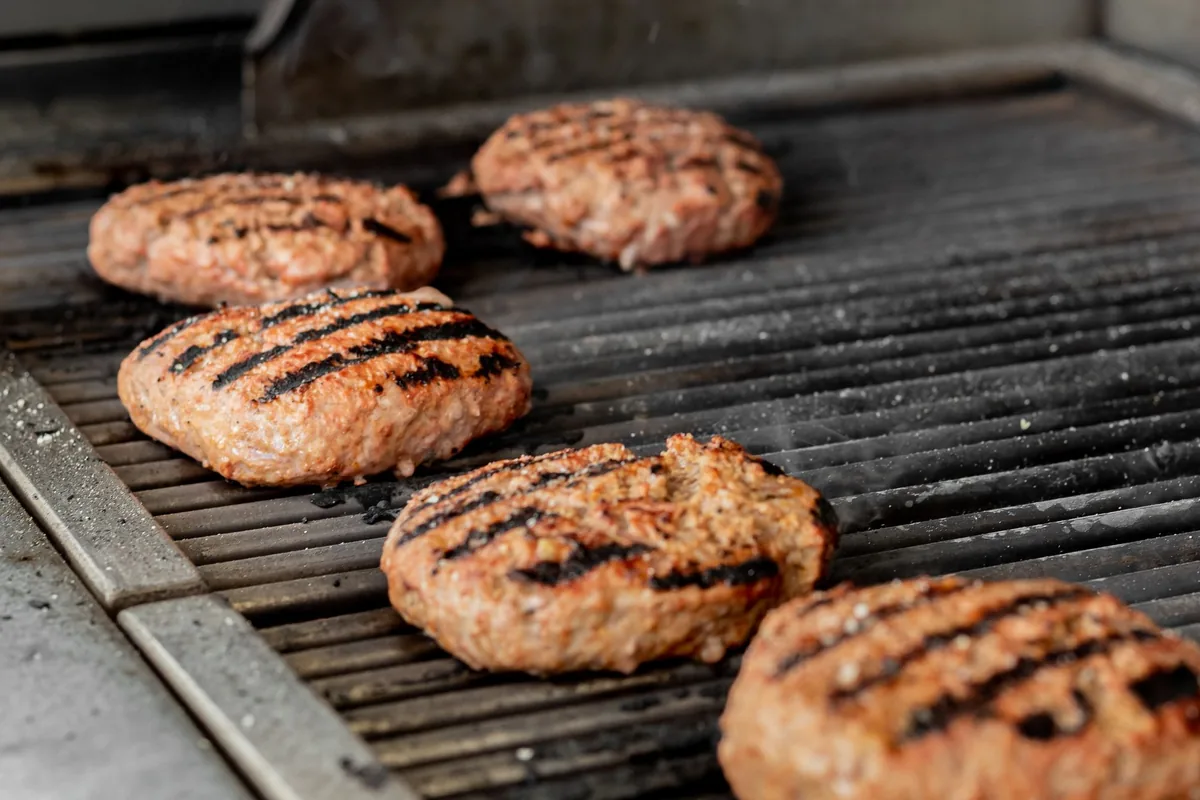 Four burger patties with grill marks on a ridged grill plate