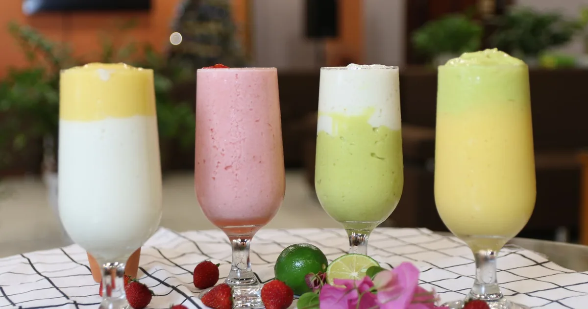 Four colourful smoothies in glasses beside fresh fruit