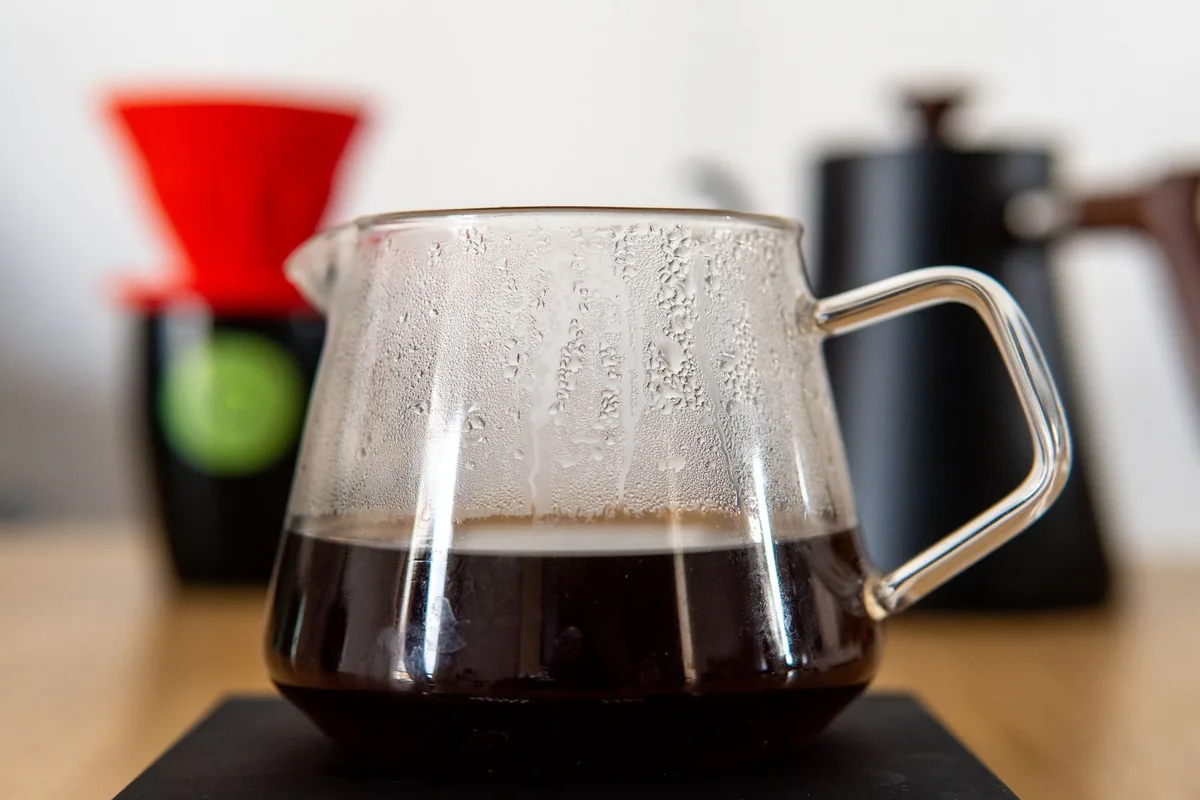 A glass carafe of brewed coffee beside a pour-over dripper and kettle