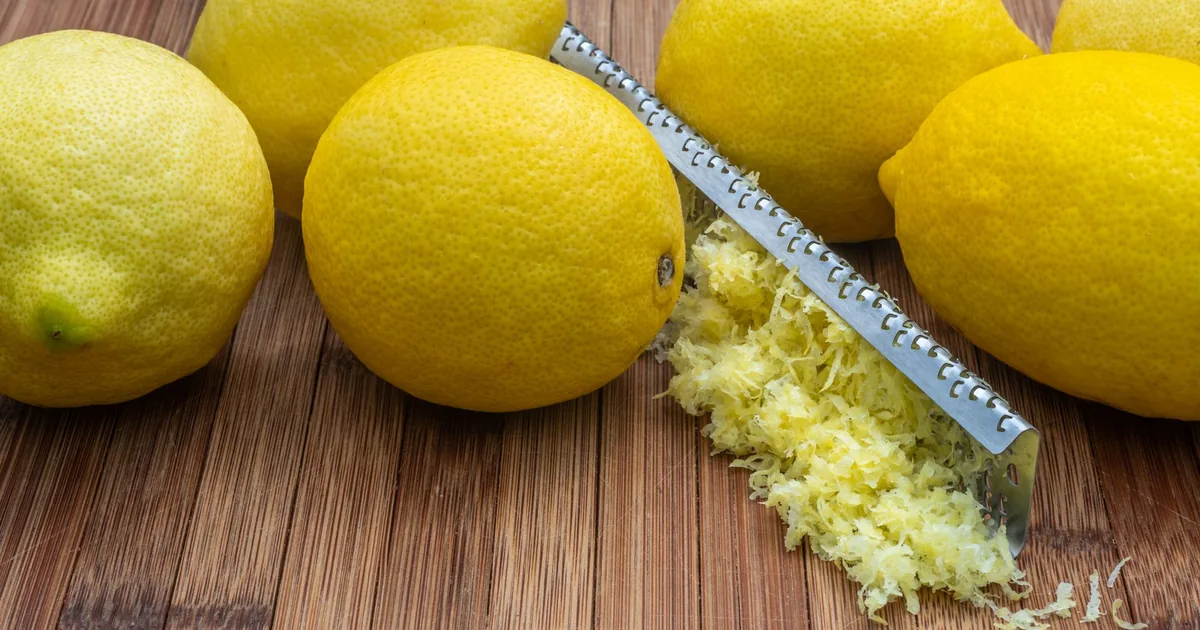 Fresh lemons beside a small pile of bright yellow grated zest on a wooden board