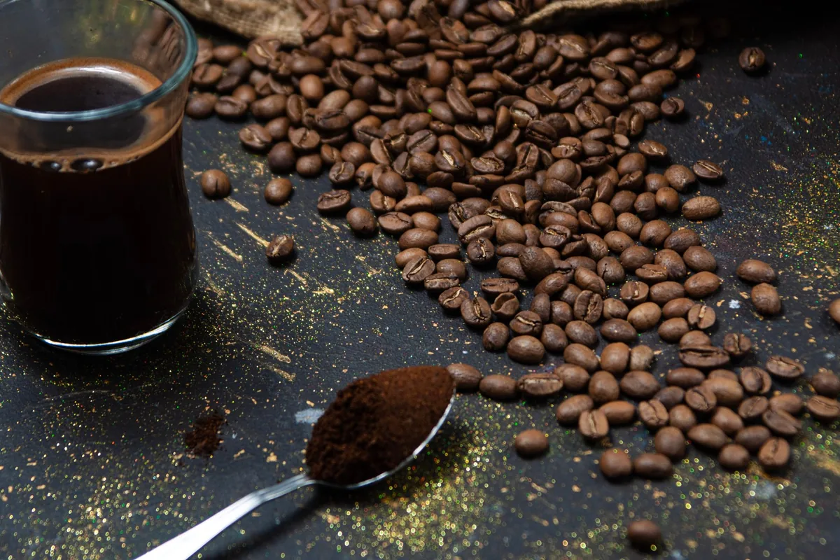 Whole coffee beans and a spoonful of ground coffee on a dark table