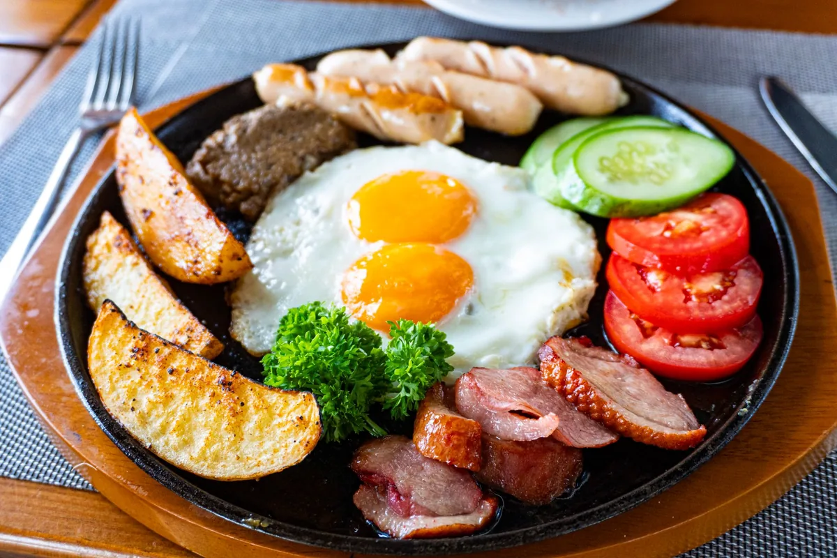 Fried eggs, sausages and potato wedges on a sizzling cast iron serving plate