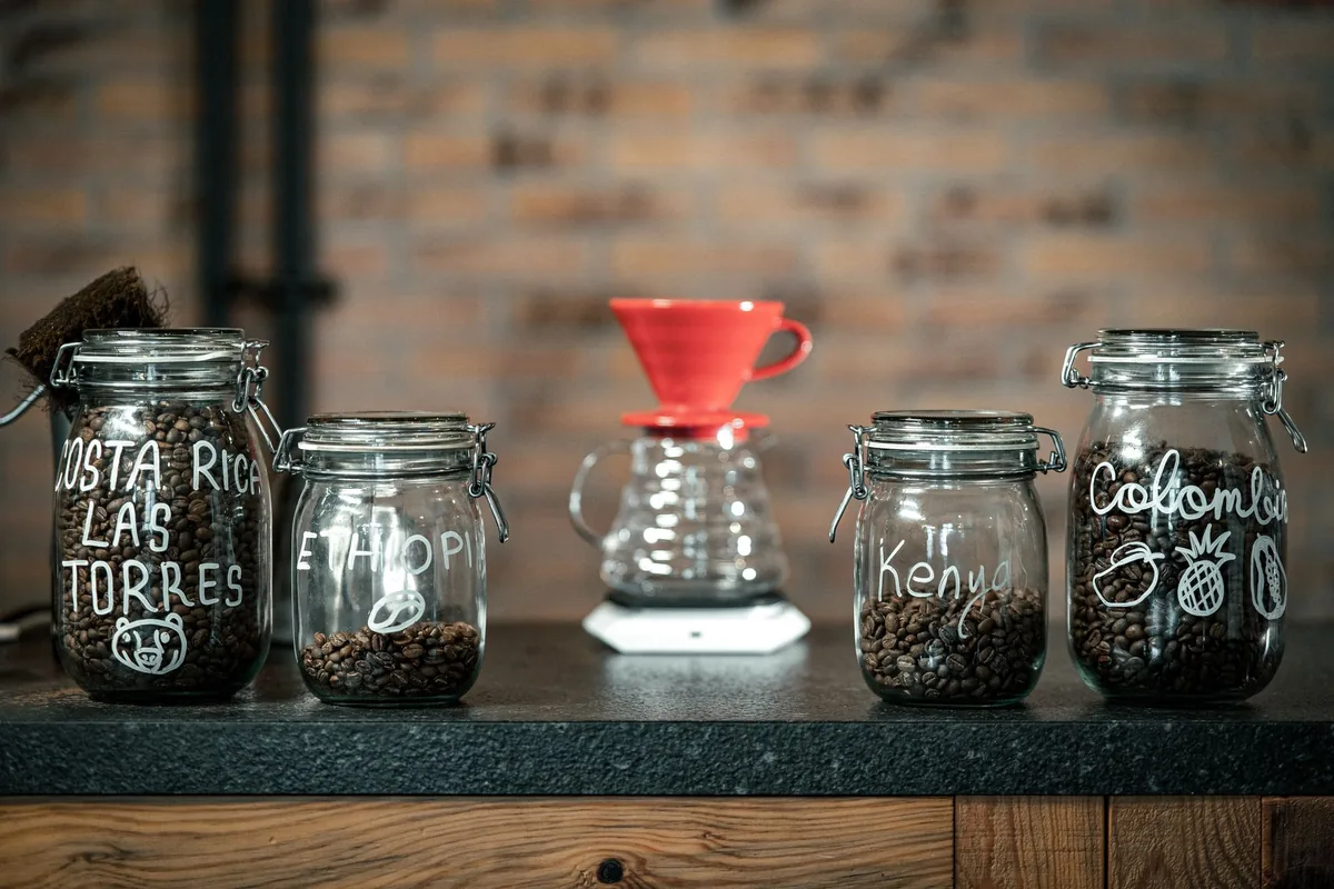 Glass jars of coffee beans beside a red dripper on a shelf