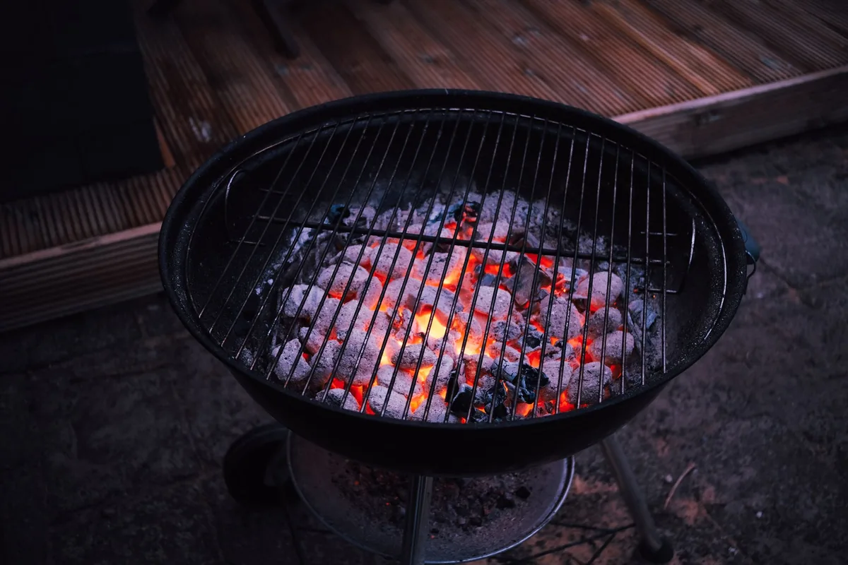 Grey charcoal briquettes heaped in the bowl of a grill in daylight
