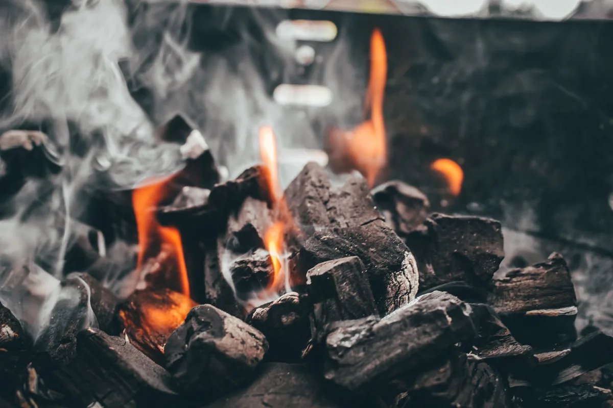 Grey-edged charcoal briquettes glowing orange in a neat pile