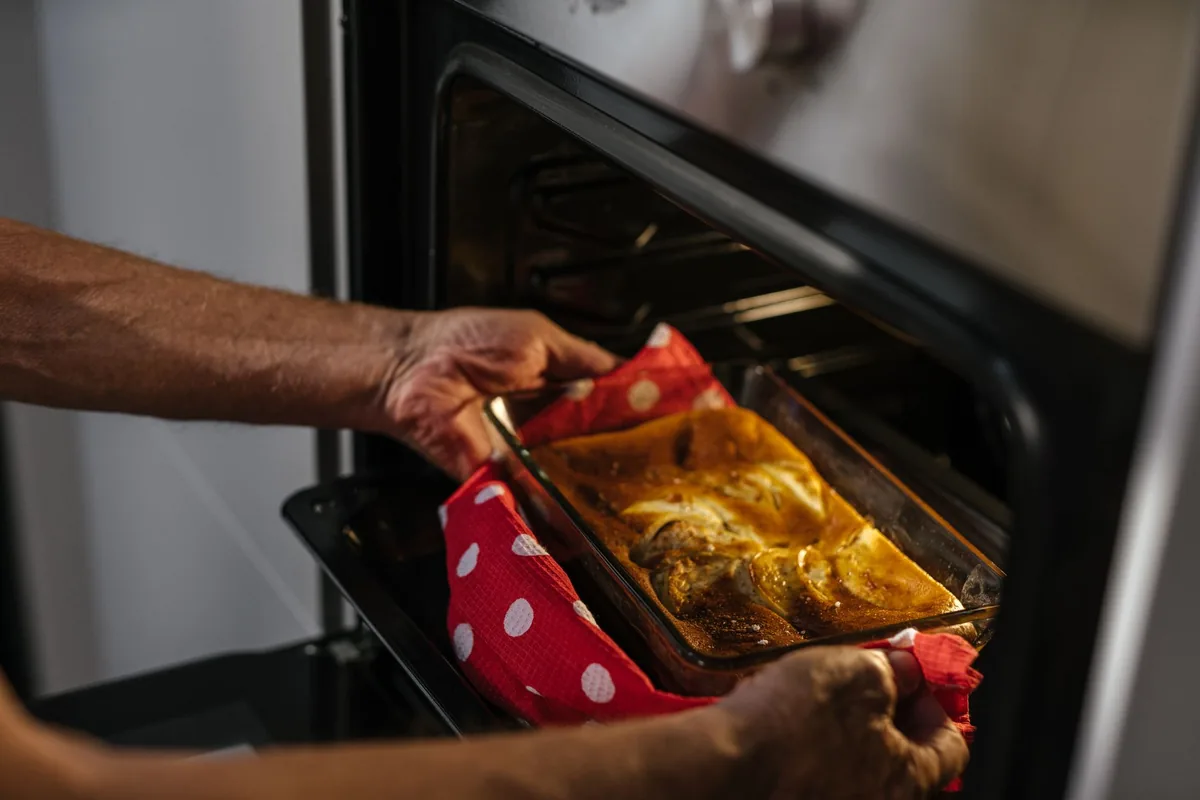 Hands in cloth oven mitts lifting a hot baking dish out of an oven