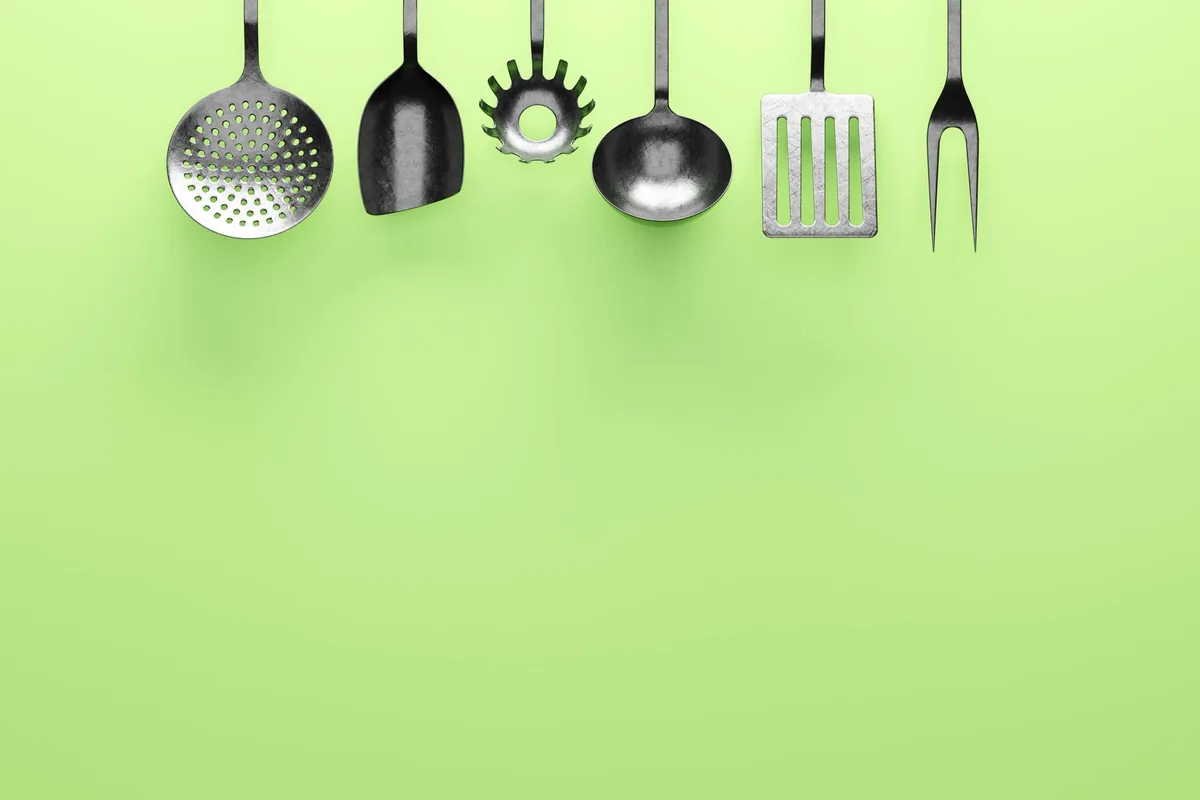 Metal kitchen utensils hanging from hooks on a rail against a light tiled wall
