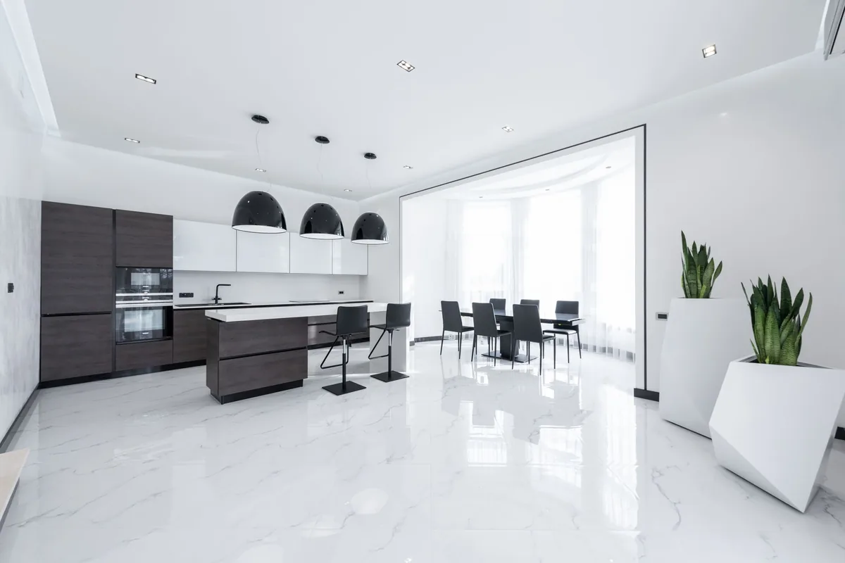 A minimalist white kitchen with a dark island and a flat ceiling