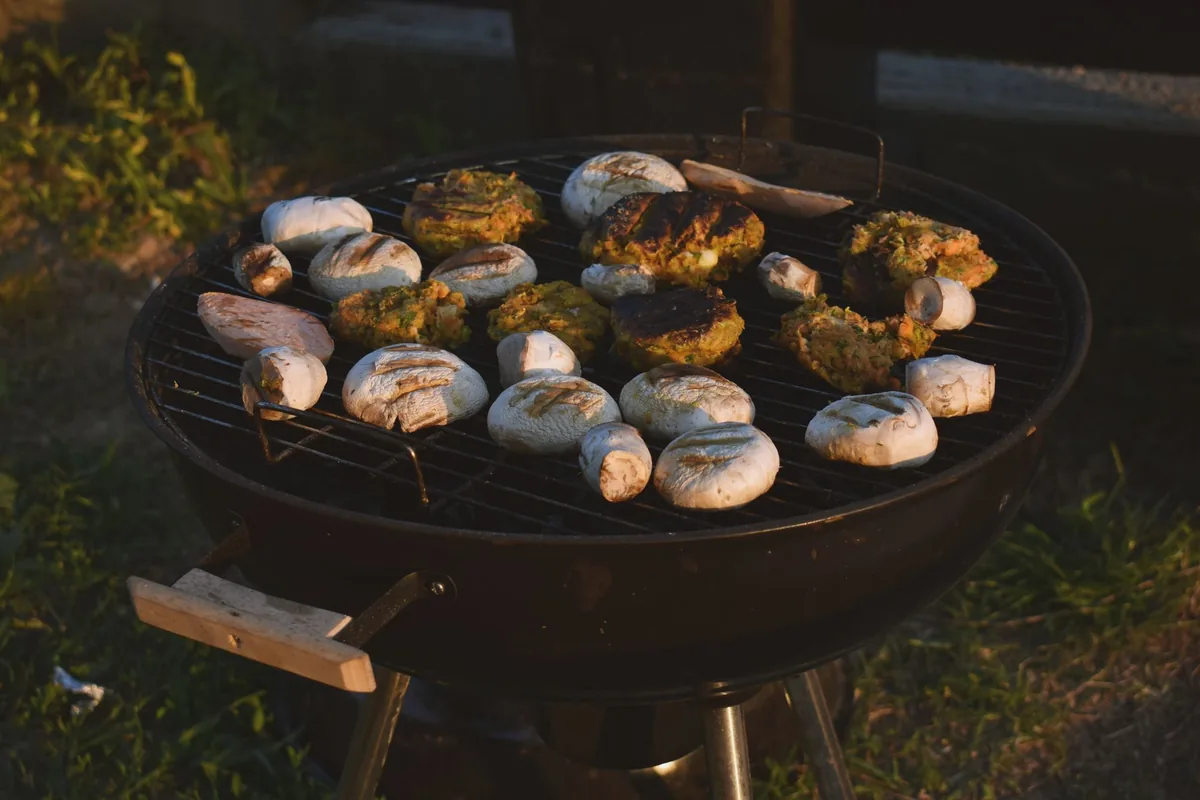Mushrooms and vegetables cooking on a round grill grate outdoors