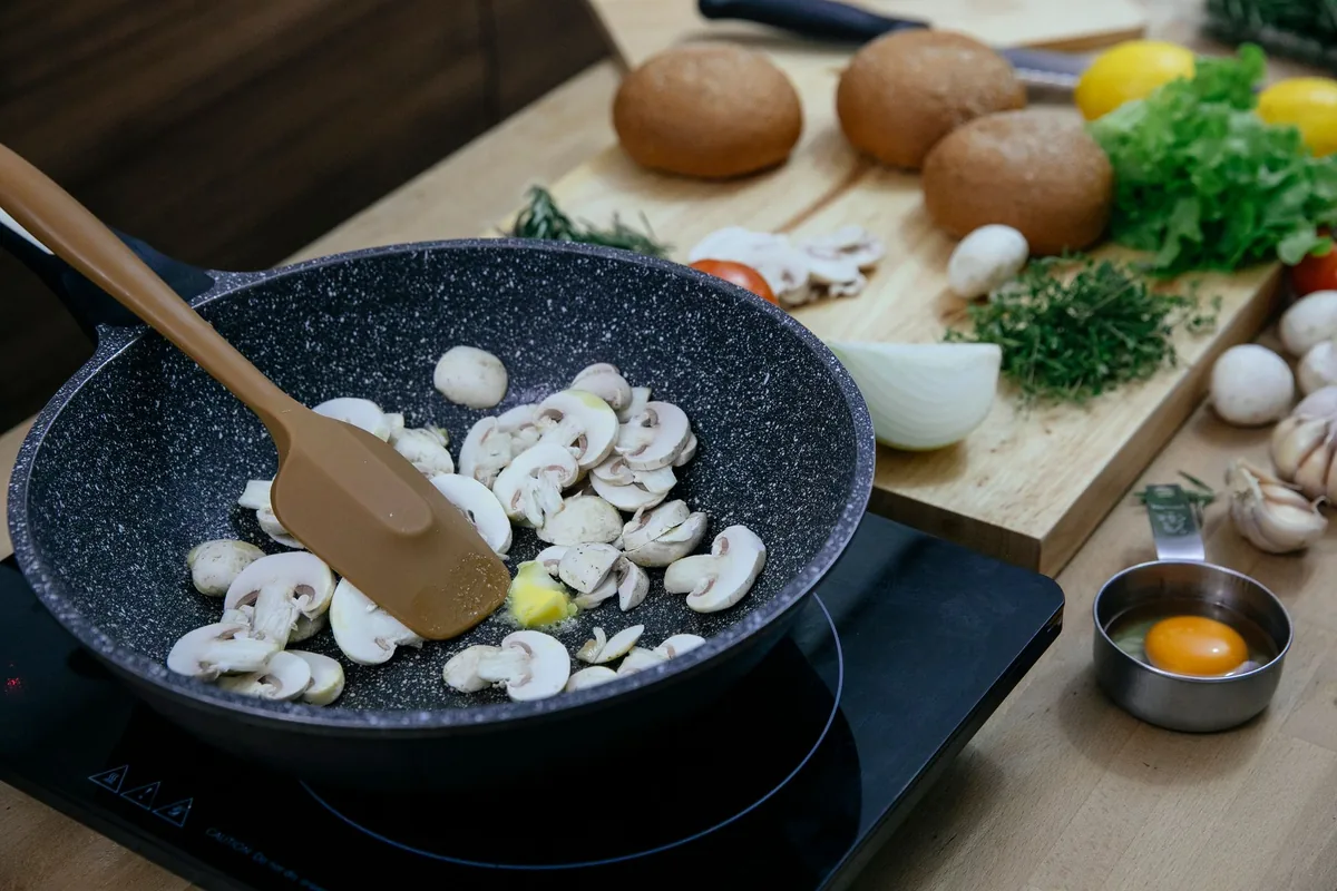 Mushrooms cooking in a dark nonstick pan with a wooden spatula