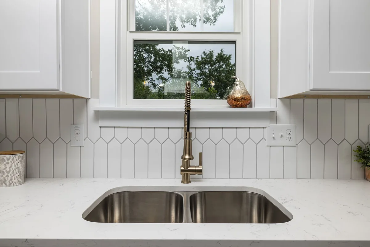 Open cabinet beneath a kitchen sink showing white supply pipes and a drain trap