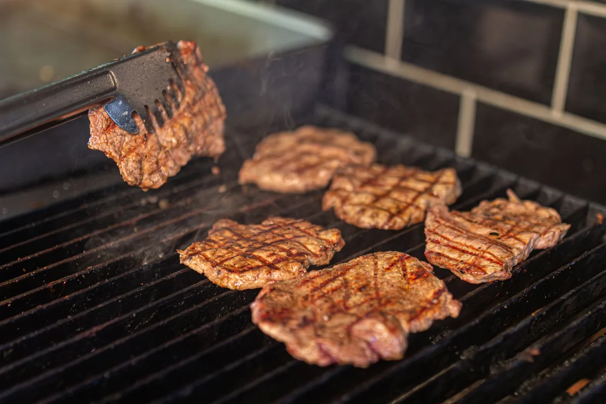Patties searing on a flat griddle beside a spatula