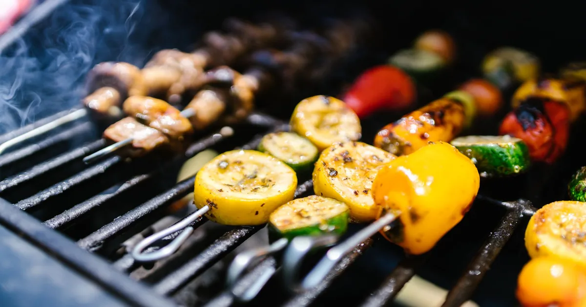 Peppers, corn and courgettes cooking on a hot barbecue grate with light smoke in daylight