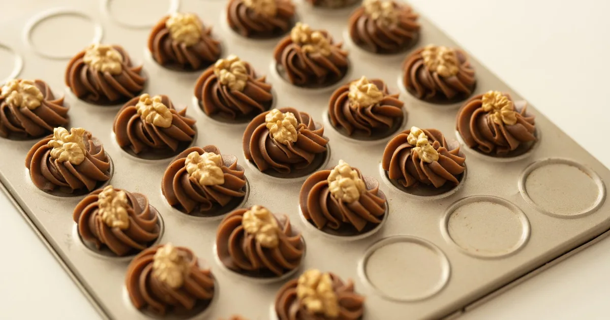 Piped chocolate cookies in rows on a baking mat