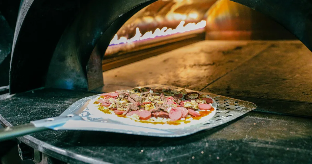 Pizza being launched into a hot outdoor pizza oven on a metal peel