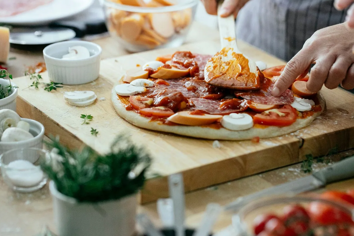 Pizza dough being topped on an outdoor prep table
