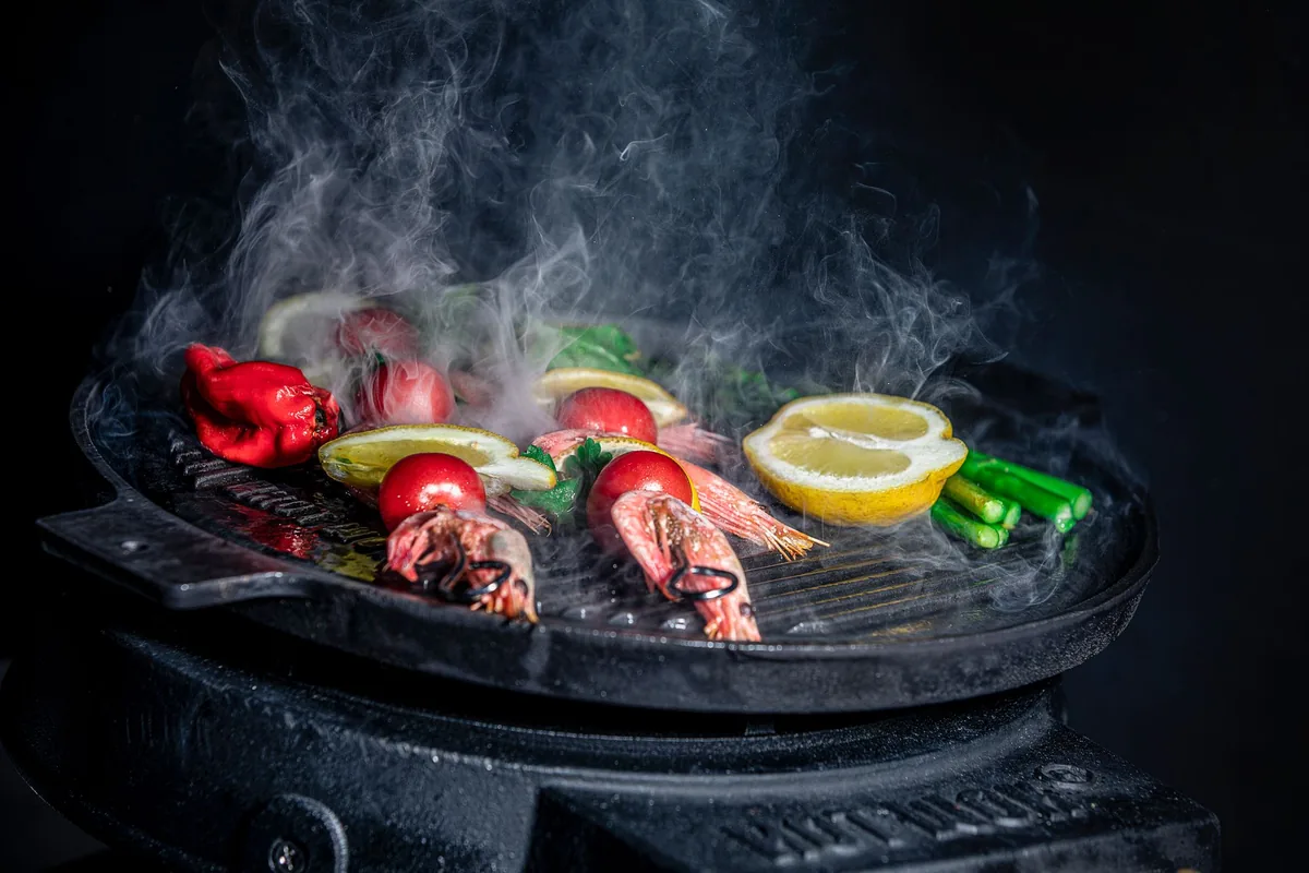 Prawns and sliced vegetables cooking on a flat griddle plate in a bright kitchen
