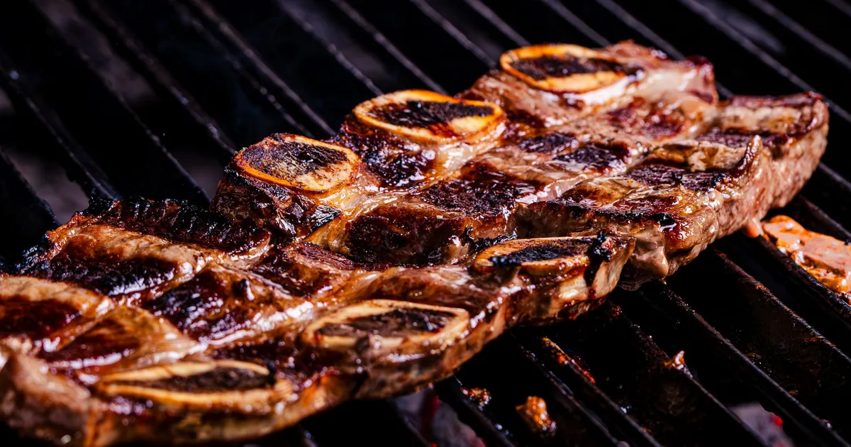 Racks of smoked ribs with a dark crust resting on a metal grill grate outdoors