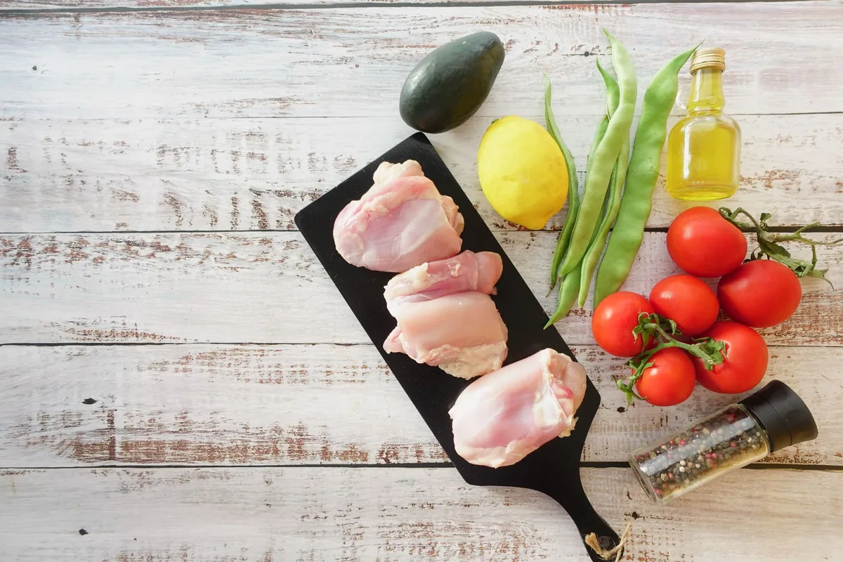 Raw chicken thighs arranged on a white cutting board in a light kitchen