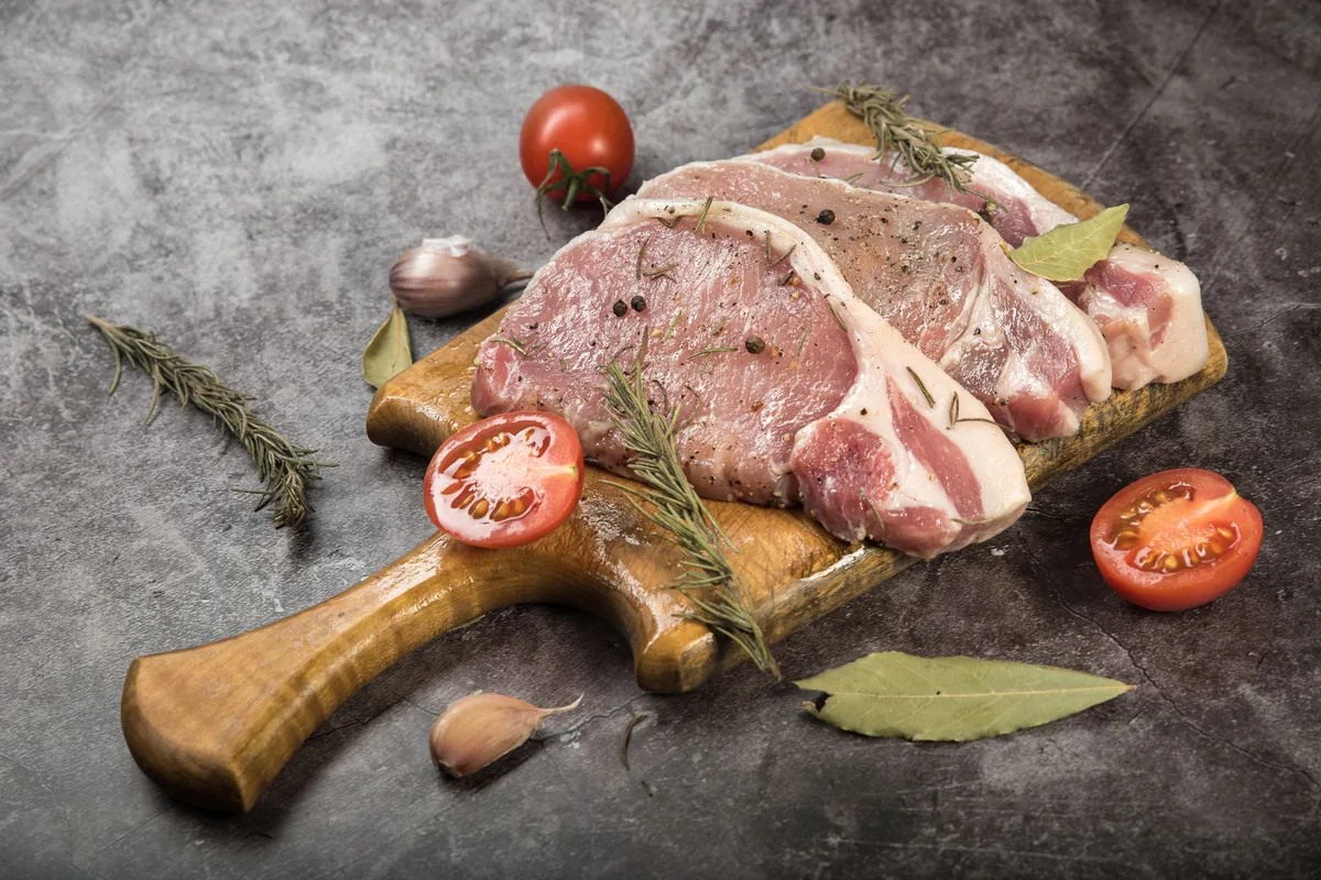 Raw pork chops with rosemary on a rustic board