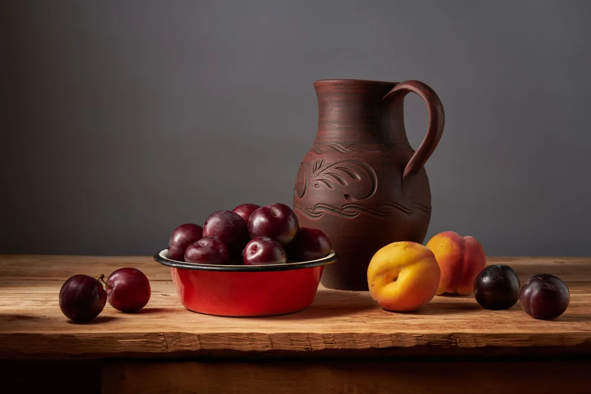 Ripe peaches and plums in a white bowl on a sunny kitchen table