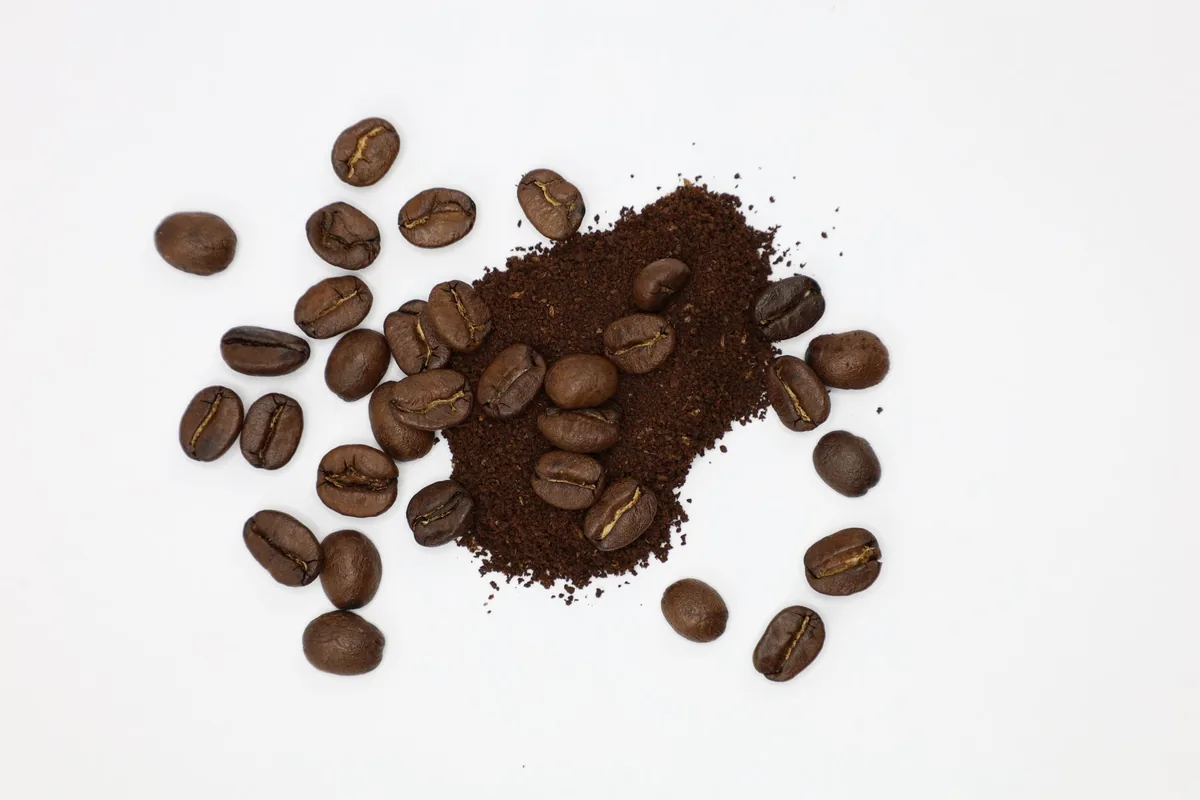 Roasted coffee beans beside a small pile of coarse ground coffee on a wooden board